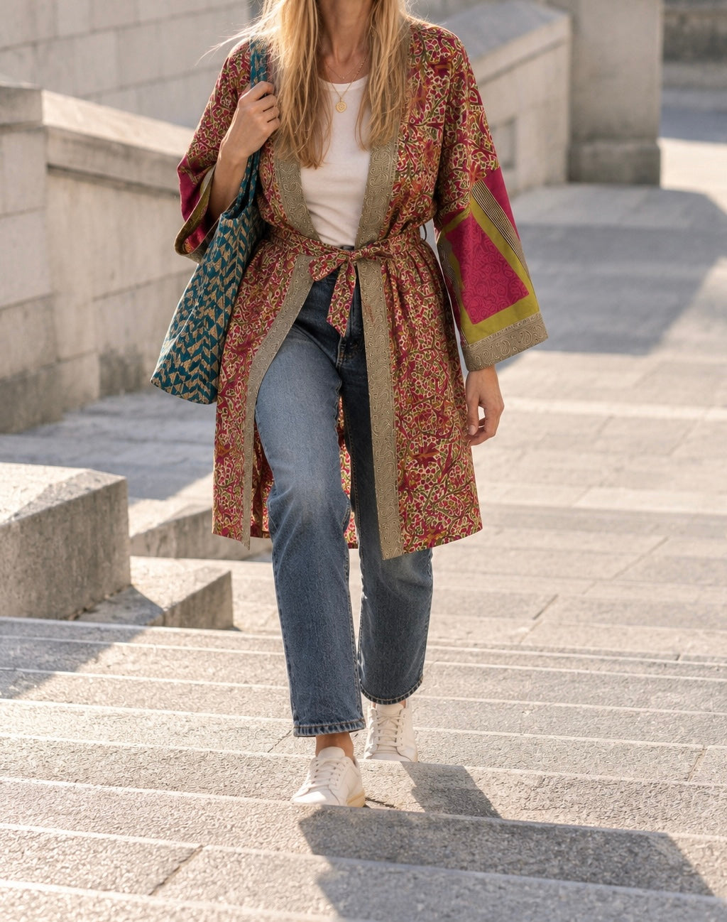 Femme portant un kimono midi en sari indien recyclé aux motifs rouges, roses et verts, associé à un jean, dans un escalier extérieur.