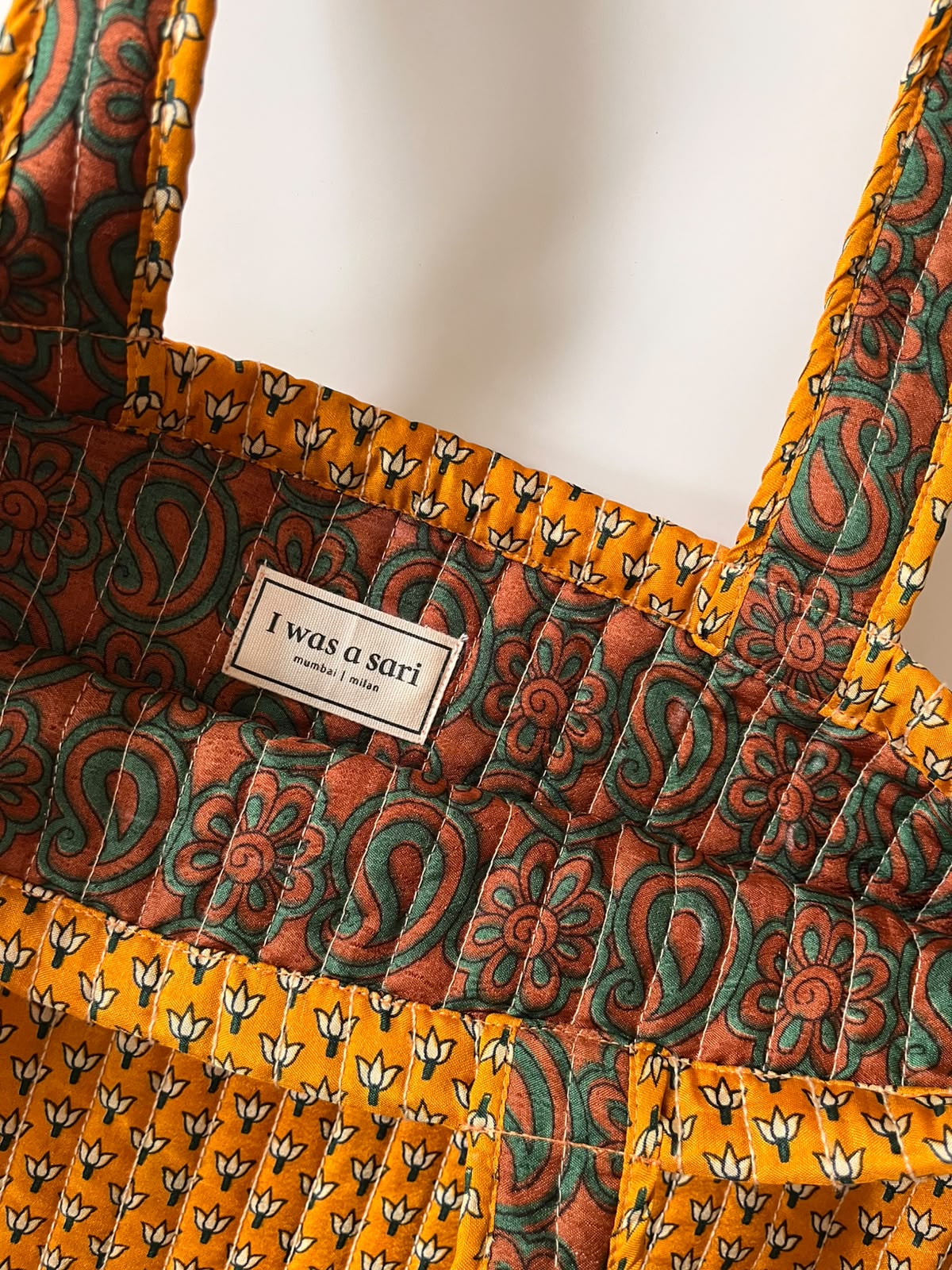 Gros plan sur le tissu d'un sac cabas en sari recyclé ocre aux finitions artisanales.