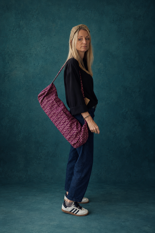 Femme portant à l’épaule un sac pour tapis de yoga en sari indien recyclé bordeaux et beige à motifs.