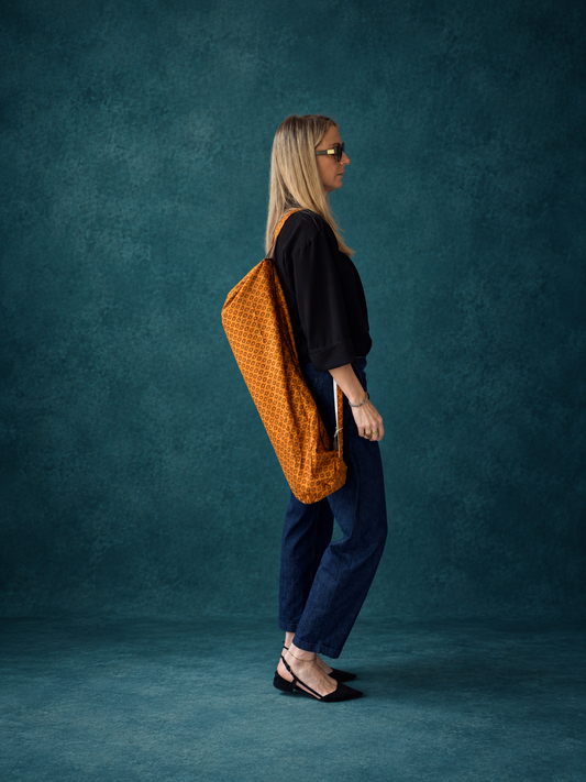 Femme portant à l’épaule un sac de yoga en sari indien recyclé orange et bordeaux.